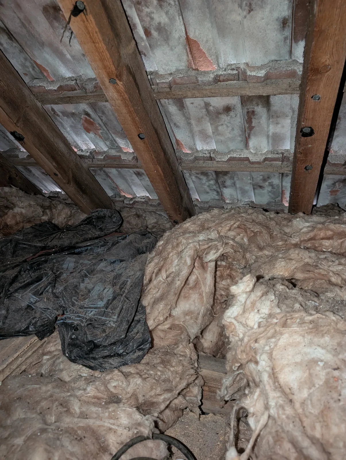 Old loft insulation heaped across the joists in a Lancing loft before loft boarding