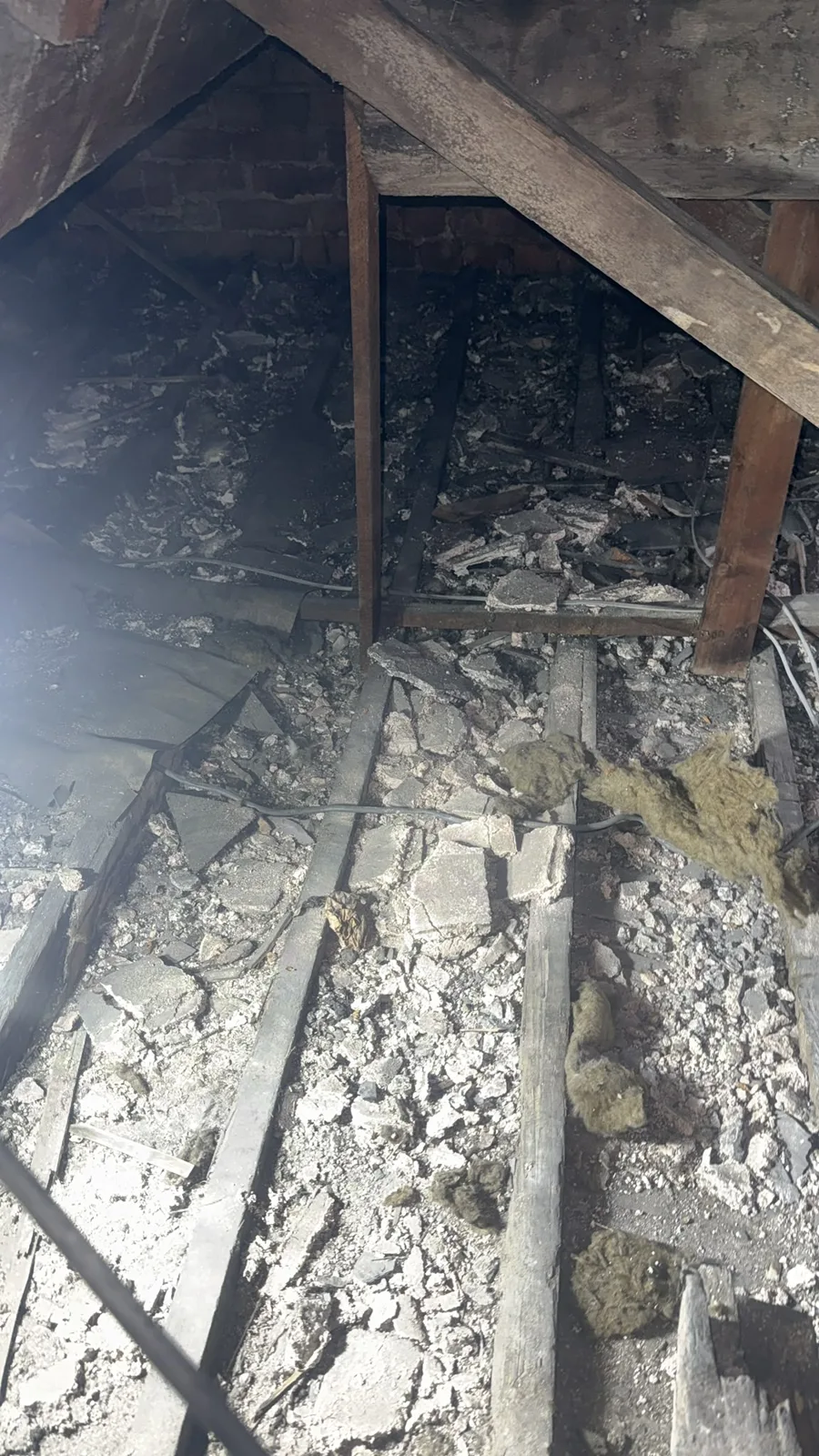 Old, debris-filled loft insulation between the joists in Denbigh before removal