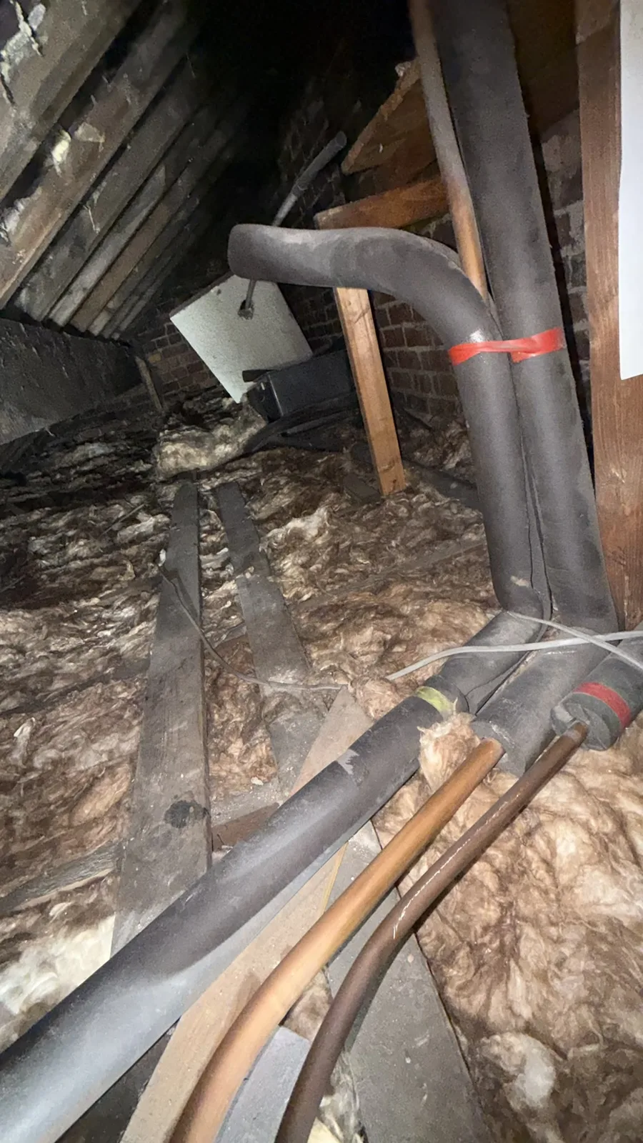 Pipework and old insulation in a Salford loft before new 300mm loft insulation